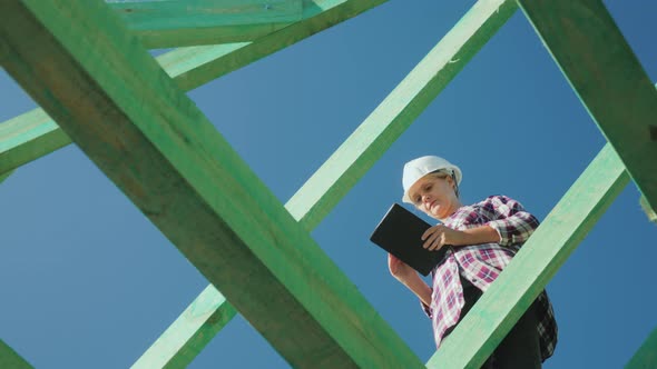 A Female Architect Is Working with a Tablet Among the Rafters of the Roof. Architectural Supervision