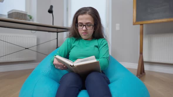 Intelligent Little Person Reading Book Gesturing I Got an Idea Smiling Sitting on Bag Chair Indoors