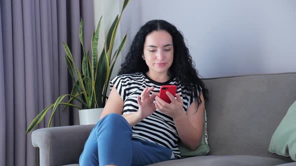 Woman Typing on Phone Sitting on Sofa at Home, Businesswoman Sits at Home Types on Smartphone Checks