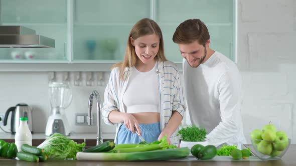 Woman Prepares a Salad in the Kitchen Cuts Herbs and Green Vegetables Young Couple on the Kitchen
