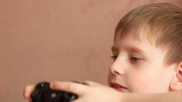 Active Caucasian preschooler boy playing game console. The child holds a game joystick in front of h