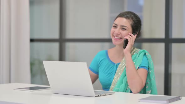 Indian Woman Talking on Phone While Using Laptop in Office