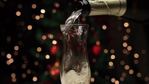 Pouring champagne in front of Christmas lights decoration in slow motion. White wine drink in flute
