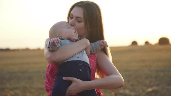 Mother Caresses Whirls and Embraces Baby Son with Harmony in Hay Field at Sunset