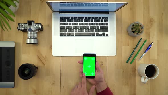Flat Lay Of Man Hands Using Phone With Green Screen At Workplace
