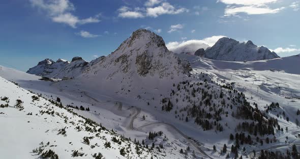 Forward Aerial Over Snowy Valley with Woods Forest and Hairpin Bend Road at Pordoi Pass