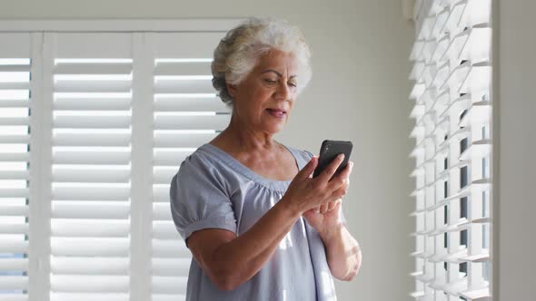 African american senior woman using smartphone and looking out of the window at home