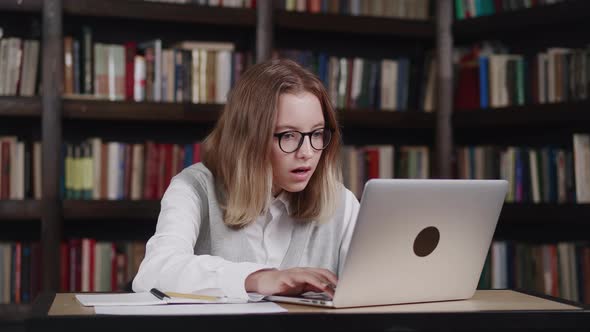 a Schoolgirl in a Gray Vest and White Shirt Looks at the Laptop Screen and Takes Off Her Glasses in