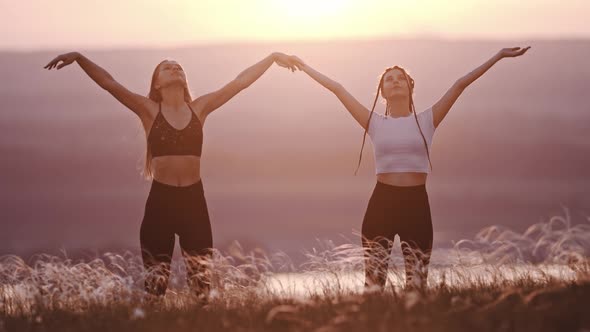 Two Young Women Doing Yoga Exercises on Sunset Field