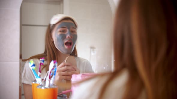 A Young Attractive Woman with a Mask on Her Face Dancing and Singing in Front of the Mirror in