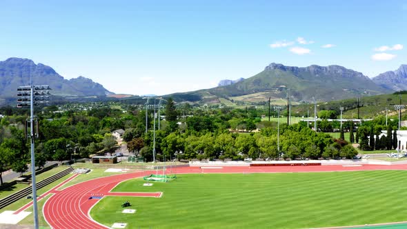 Aerial drone rotating tartan athletic track, athletes training sprints, mowing grass, university col