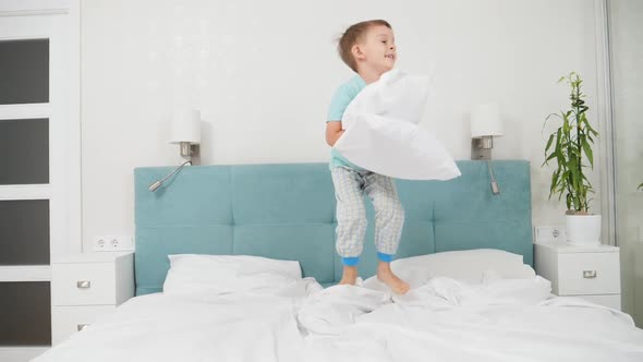 SLow Motion of Cheerful Toddler Boy Holding Pillow and Jumping Up High on Bed at Parent's Bedroom