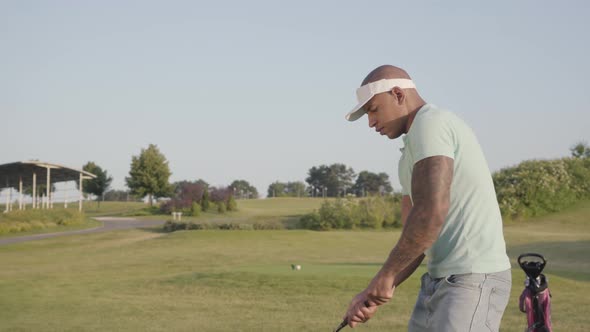 Young Concentrated Middle Eastern Man with Tattoo on the Shoulder Playing Golf on the Golf Field