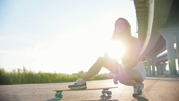 Young Attractive Woman Sitting Near the Skateboard Under the Bridge - Bright Sunlight on a Sunset