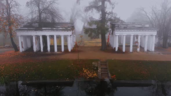 Aerial Drone Shot of Ruins and Colorful Trees Near Small Lake in Fog in Autumn Park