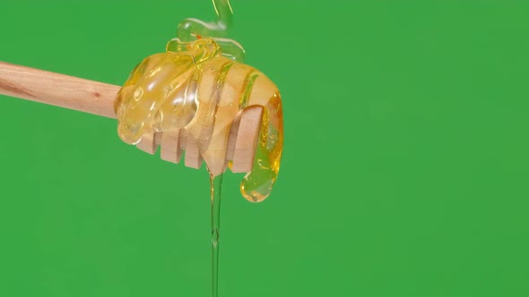 Fresh Honey Pouring and Flowing From Wooden Dipper Spoon on Green Background