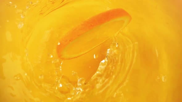 Orange slices fall into the water on an orange background. Slow motion.