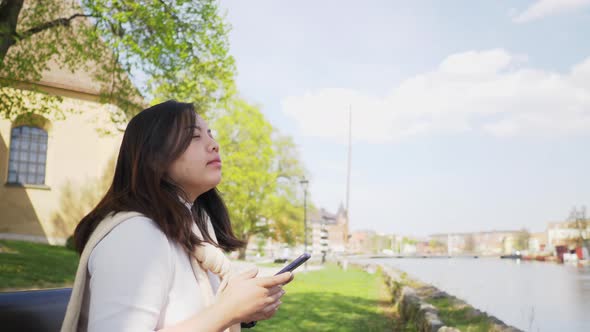 Asian woman sitting on a chair and spending time to use phone and take a deep breath at park