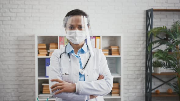 Mature Doctor Female in Protective Mask and Face Shield is Looking at you Standing at Cabinet of
