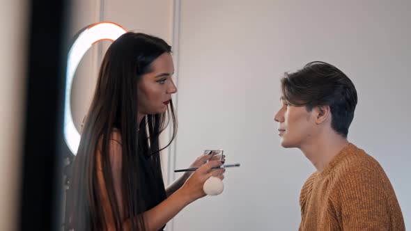 Woman Make Up Artist Applying Soft Nude Eyeshadows on the Eyes of Male Model Using a Brush