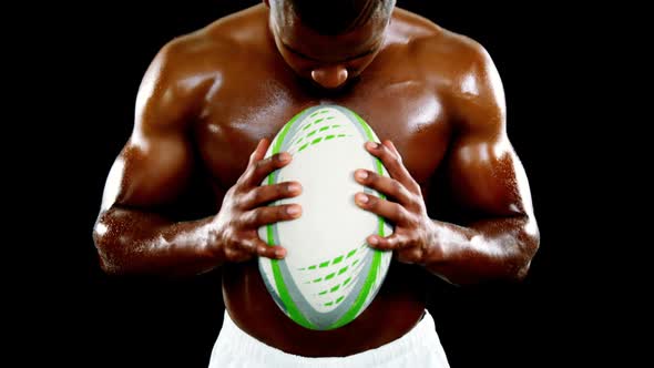 Professional rugby sportsman holding a ball against black background