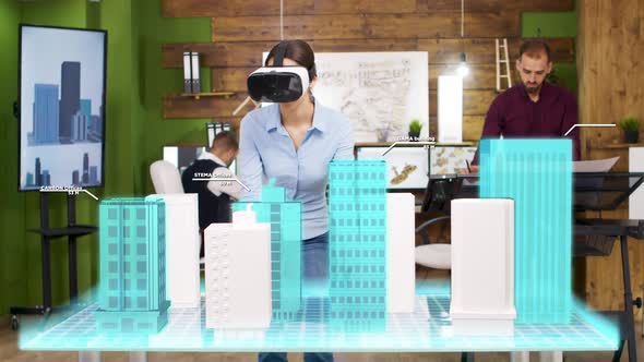 Architect Woman Wearing VR Headset Is Looking at Holographic Projections of Building a City