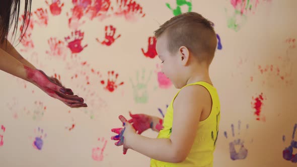 Happy Mother and Her Cute Boy Having Fun Together Leaving Their Colorful Handprints on the Wall