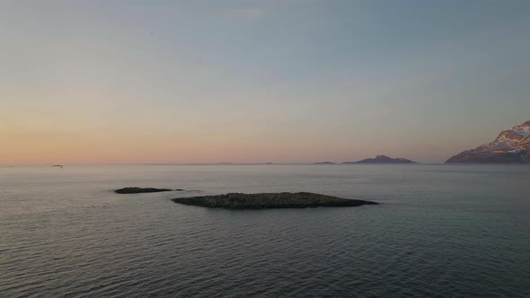 Drone pullback from rocky islands in ocean at sunset, chased by Oystercatchers