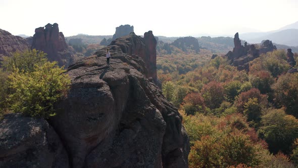 Aerial fly around a young woman standing at the adge of stunning rock formation