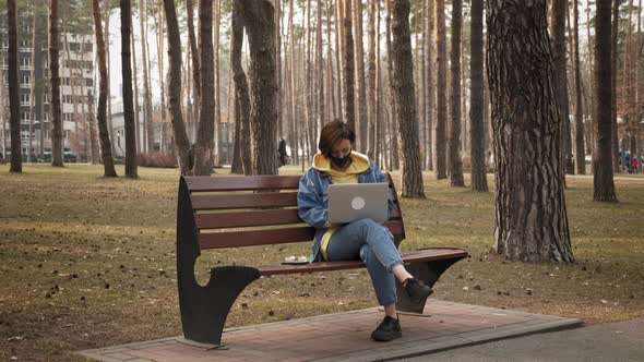 Woman working with laptop sitting on bench in  street in public park