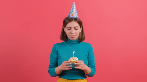 Young Woman in Birthday Hat Blowing Out Candle on Cake Isolated on Red Background