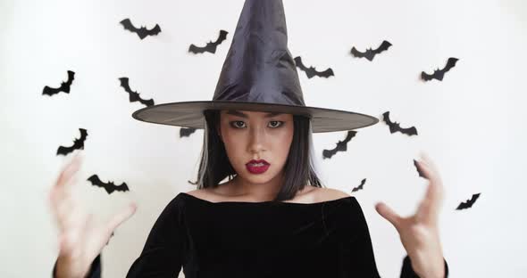 Asian Woman in Black Witch Costume Casting Spell To Camera, Halloween Magic Concept