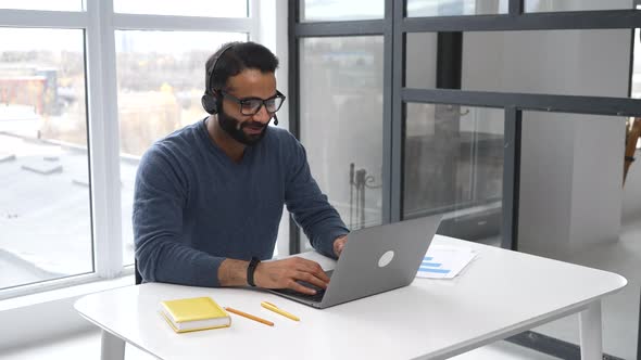 Smiling Indian Office Worker in Glasses and Headset Talking Online