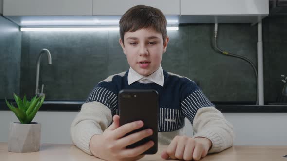 13 Years Old Boy Making Video Call Using Smartphone While Sitting at Table at Home Kitchen