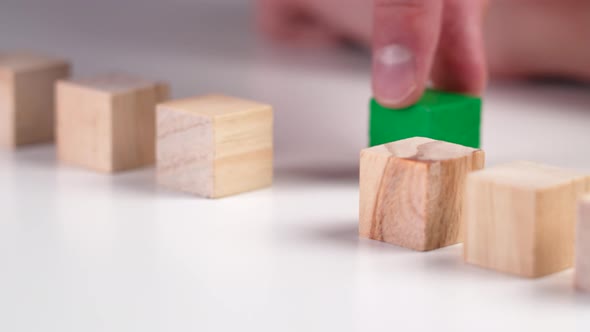 Hand moves green wooden block, stacking geometric wood cubes in a row
