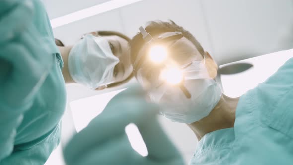 Surgeon with Nurse Are Looking Down at Camera. Handsome Young Doctor in Surgical Mask Is Holding