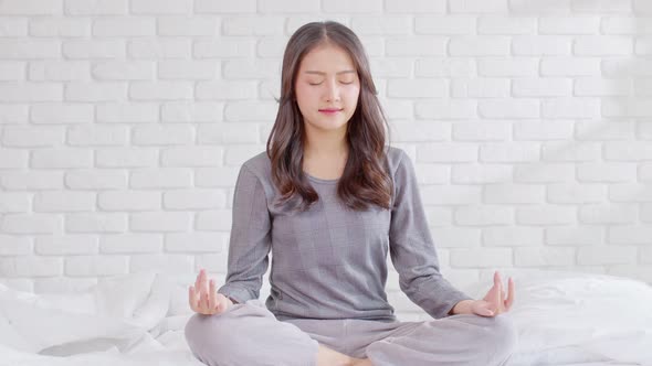 Calm of wellness Asian young woman sit on bed breathing with yoga lotus pose,