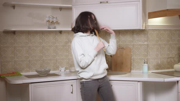 Brunette Girl Dancing and Singing in Front of the Kitchen with a Wooden Spatula