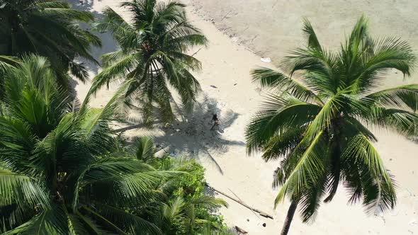 aerial top down drone view of a young asian female tourist walking on a white sand tropical beach ap