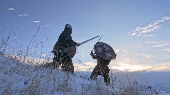Two viking are fighting with axes and shields on the winter meadow