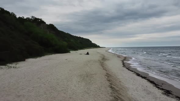 Man is Sitting on the Shore of the Ocean and Enjoying the Landscape Filmed By Drone