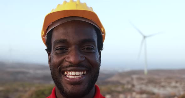 African engineer worker smiling on camera with windmill farm in background