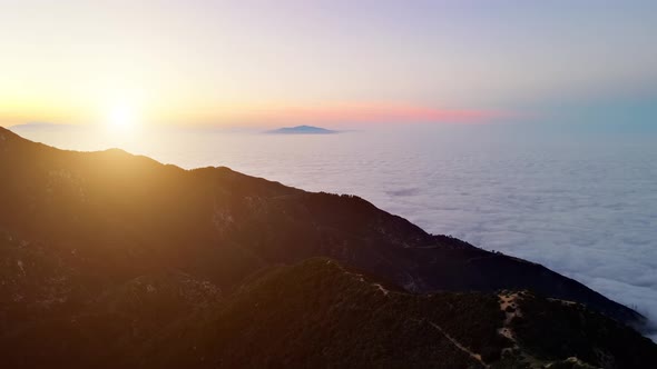 Aerial of mountains above low clouds at dawn