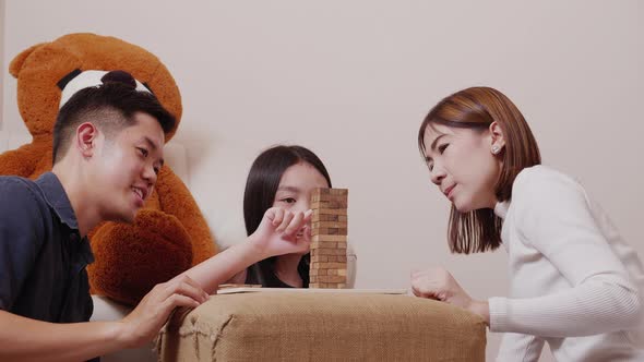 Asian mother, father, and pretty daughter playing wooden block tower together