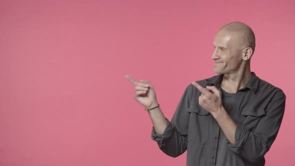 Satisfied Happy Handsome Elderly Bald Man Grandfather Showing Way Pointing Fingers Left Side of Pink