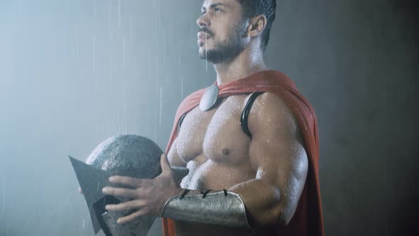 Wet Spartan Holding Helmet Under Rain.