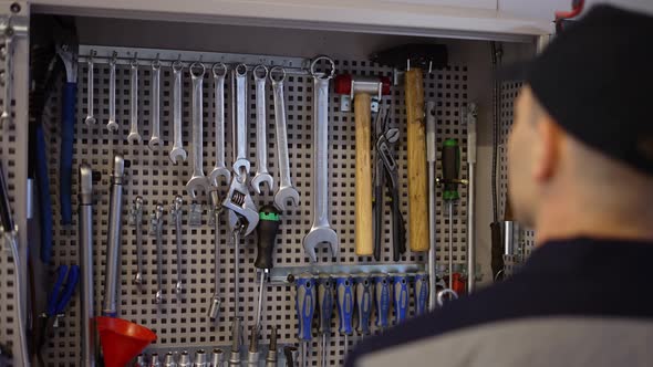 A Car Mechanic Stands Near the Stand with Wrenches Take the Required Size Slow Motion