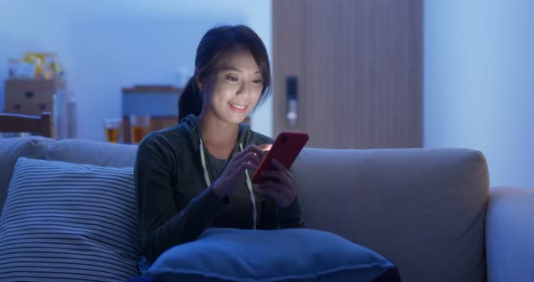 Asian woman use of cellphone sit on sofa at home in evening