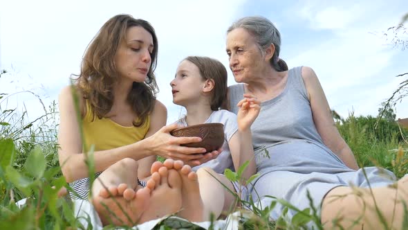 Cute Child Girl with Her Young Mother and Senior Grandmother are Having Picnic During Summer Outdoor