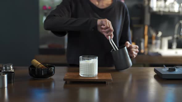 4K Asian woman barista making iced matcha green tea latte serving to customer at cafe